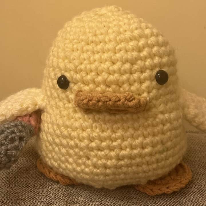 Phone photo of a crochet duck plushie on a blanket in warm indoor light